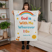 Woman holding a blanket with 'God is With Me Wherever I Go' text in a living room.