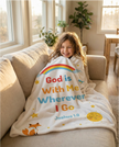 Child sitting on a couch with a blanket featuring 'God is With Me Wherever I Go' text.